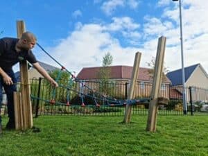 An inspector in a black polo shirt checking ropes on a piece of timber play equipment